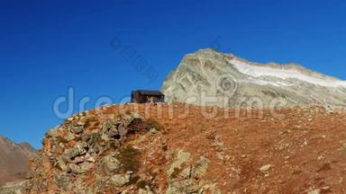 女人到达山顶上的山屋，在高空岩石景观中，背景是冰川和山峰。 历险记